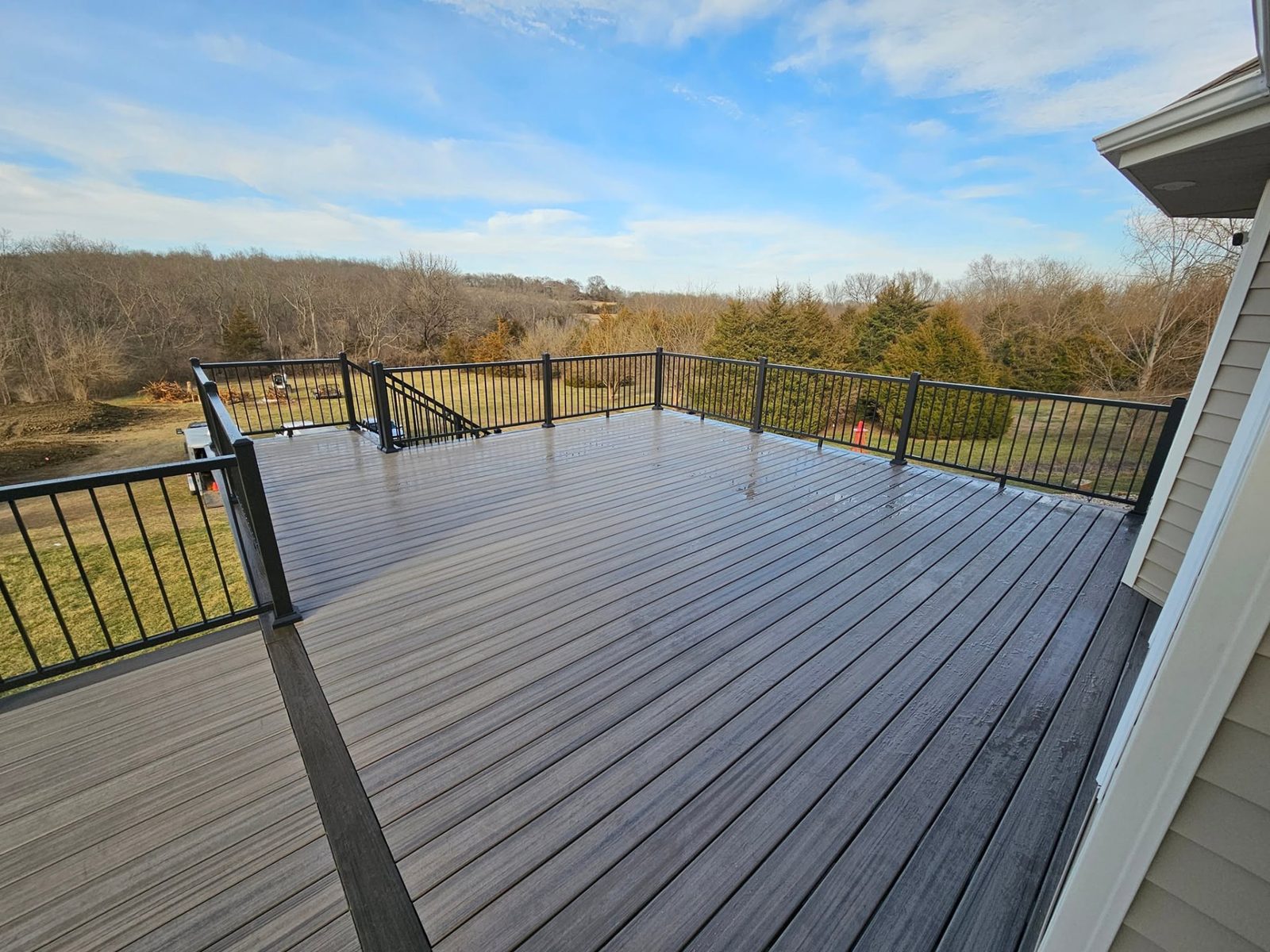 Wide composite deck with black aluminum railing overlooking an open Kansas tree line